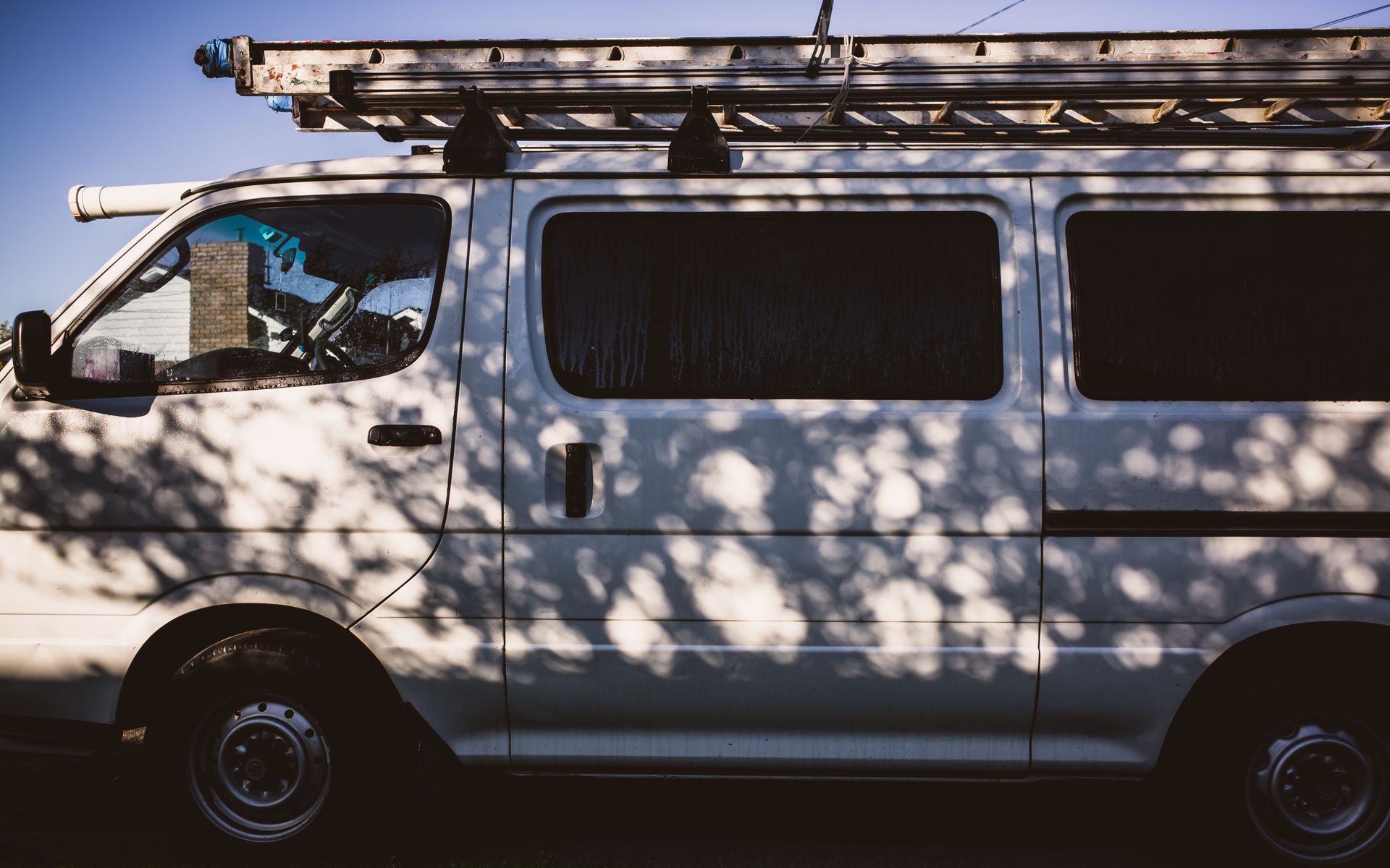 White work van with a ladder on the roof racks