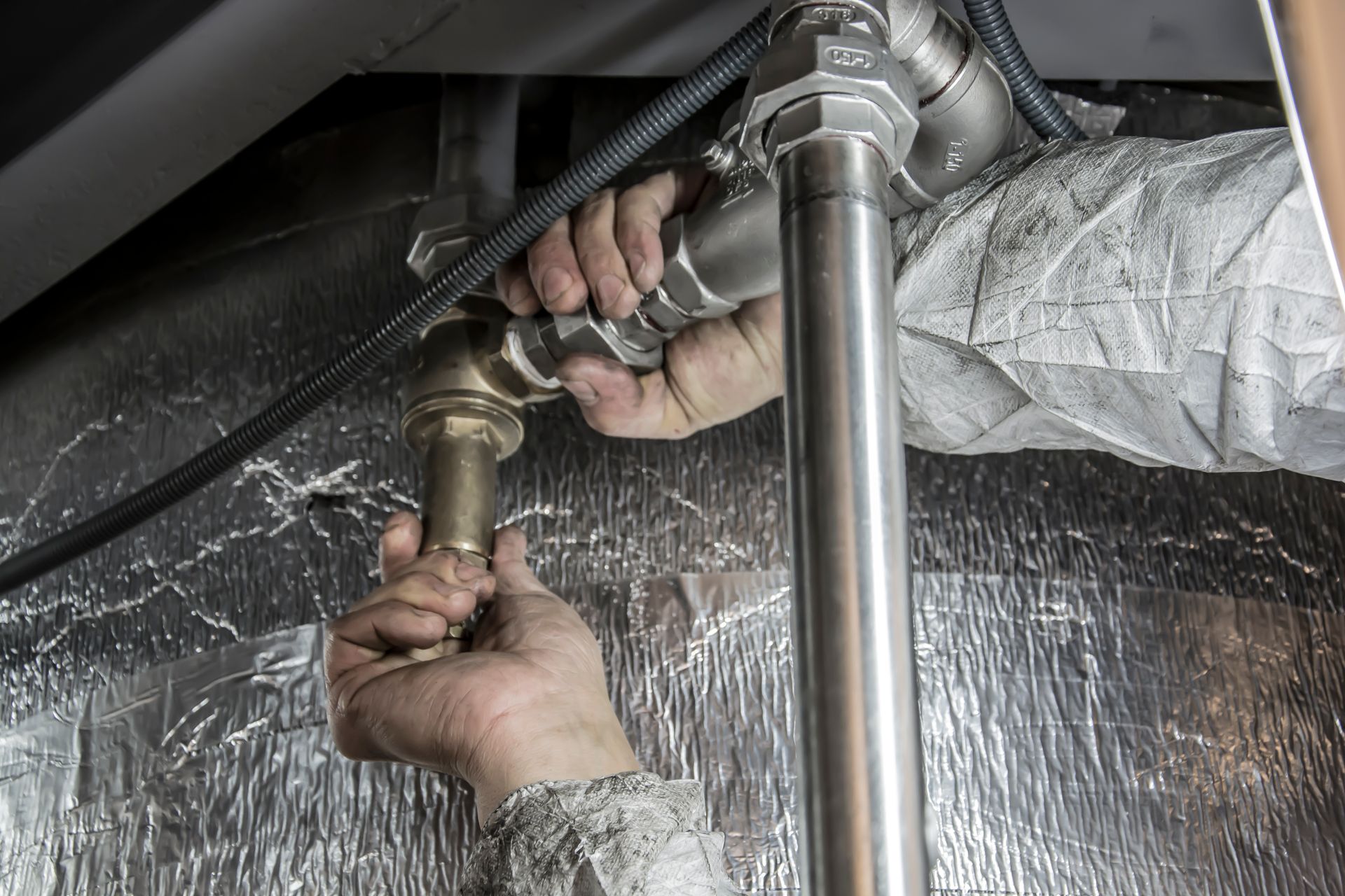 Plumber's hands tightening a pipe fitting under a unit